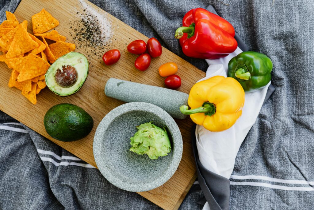 Colorful ingredients including avocados, bell peppers, and nachos for making fresh guacamole.